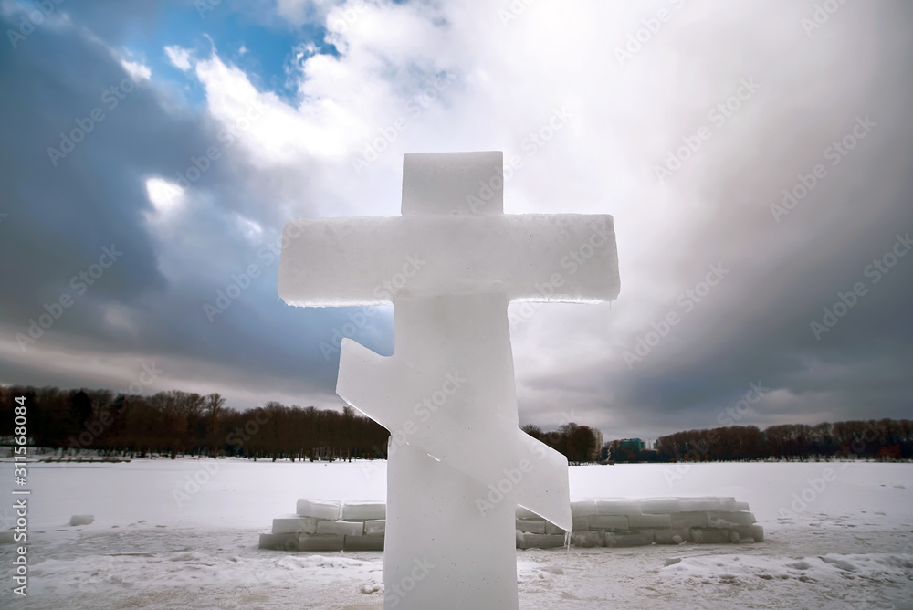 Christian cross made of ice near the ice hole in river. Holidays of Orthodox baptism. Concept of swimming in cold water. Saint Epiphany - Religious feast Christian cross made of ice near the ice hole in river. Holidays of Orthodox baptism. Concept of swimming in cold water. Saint Epiphany - Religious feast