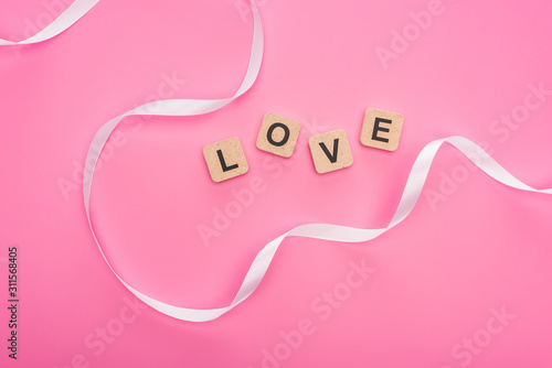 top view of curved ribbon and wooden blocks with love lettering isolated on pink