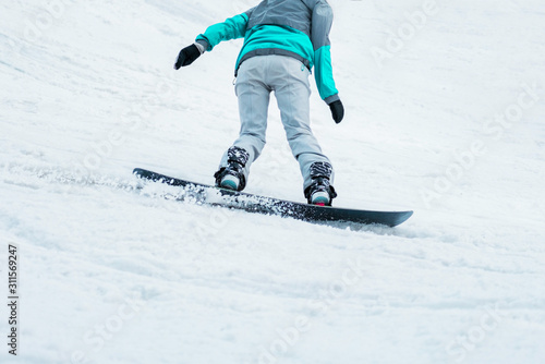 Woman in a turquoise jacket and gray pants snowboarding on a black board. Winter sports. Snow. Sport. Cold. Weather. Rider. Season. Equipment. Slope. Mountains photo