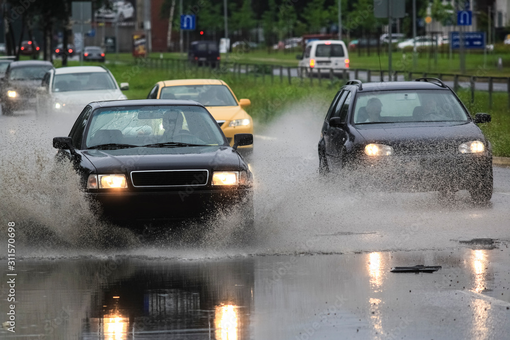 driving car on flooded road during flood caused by torrential rains. Cars float on water, flooding streets. Splash on the car. Flooded city road with a large puddle driving car on flooded road during flood caused by torrential rains. Cars float on water, flooding streets. Splash on the car. Flooded city road with a large puddle