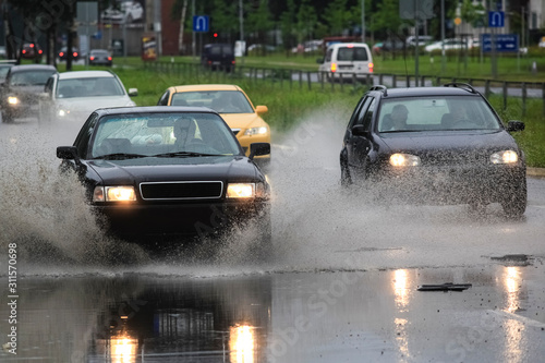 driving car on flooded road during flood caused by torrential rains. Cars float on water, flooding streets. Splash on the car. Flooded city road with a large puddle