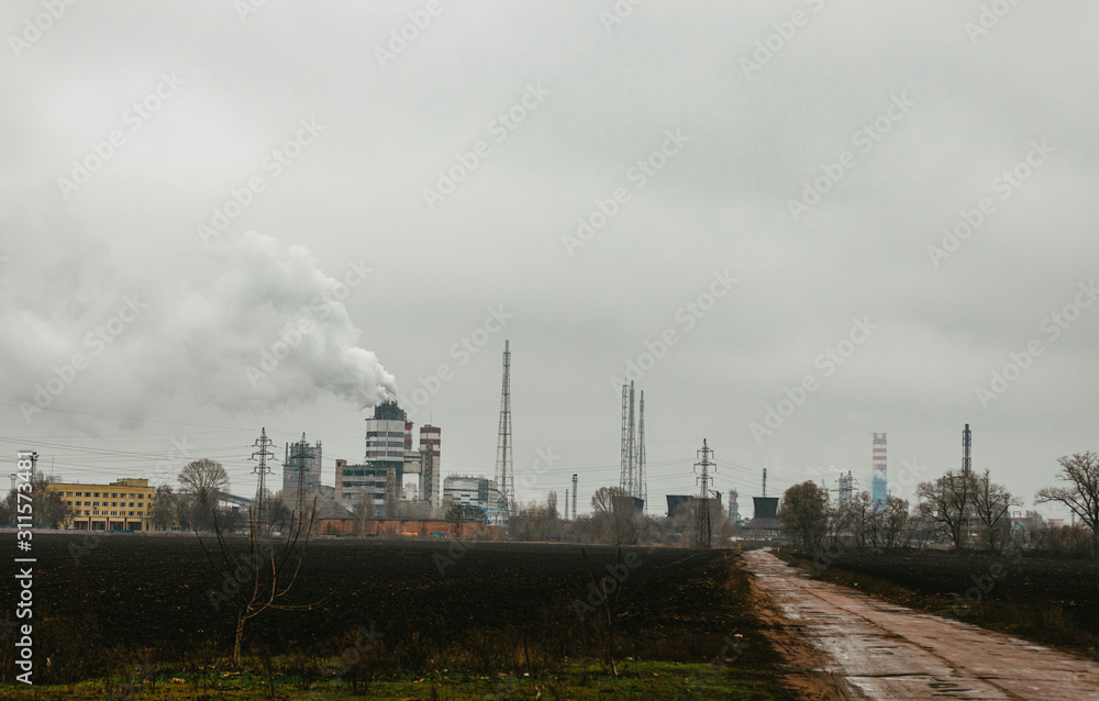 Late autumn landscape with an industrial enterprise on the horizon. Gloomy cloudy day, plowed field and old broken road in the foreground. Late autumn landscape with an industrial enterprise on the horizon. Gloomy cloudy day, plowed field and old broken road in the foreground.