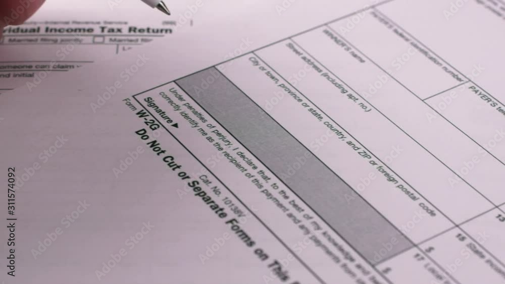 Tax reporting. Human fills out Tax Form W-2g, puts a signature. Close-up