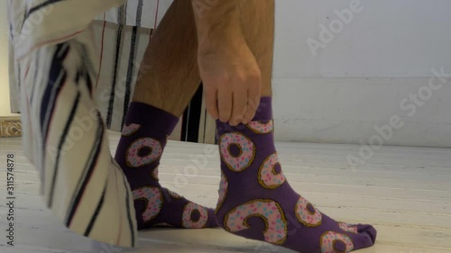 A man pulls funny print socks on his legs. Early morning