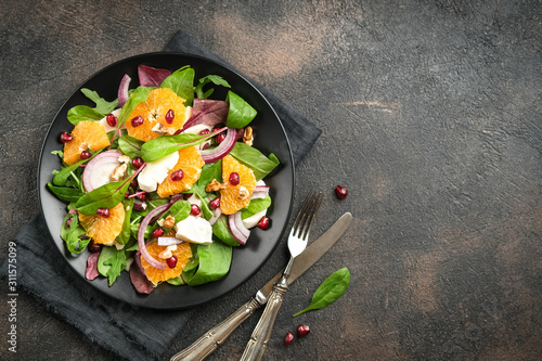 Detox salad with tangerines, mozzarella, herbs, pomegranate seeds and nuts on a dark background. Free copy space.
