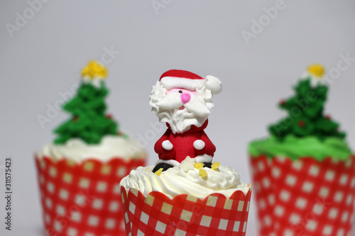 Christmas cupcakes decorated with Santa Claus and out focus Christmas tree cupcakes.