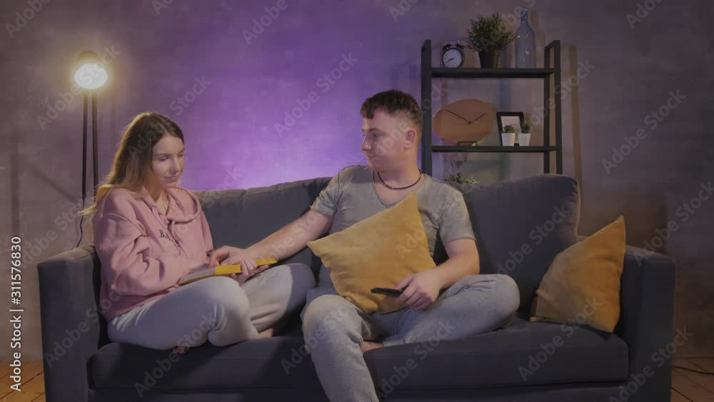 A man watches TV. Beautiful girl reading a book near to her husband A man watches TV. Beautiful girl reading a book near to her husband
