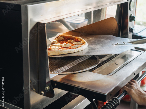 Cooking in modern pizza oven in cafe kitchen