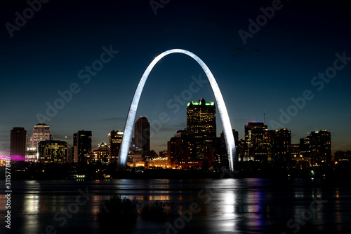 St Louis Gateway Arch brightly lit and shining at night, city skyline in background, reflecting in Mississippi River 