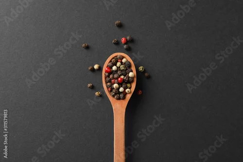 Obraz drewniana łyżka z kolorowymi ziarnami pieprzu na ciemnym tle