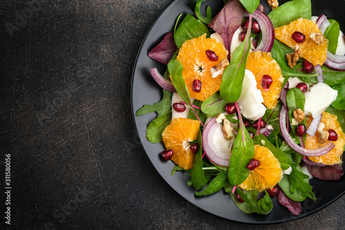 Detox salad with tangerines, mozzarella, herbs, pomegranate seeds and nuts on a dark background. Free copy space. Top view.