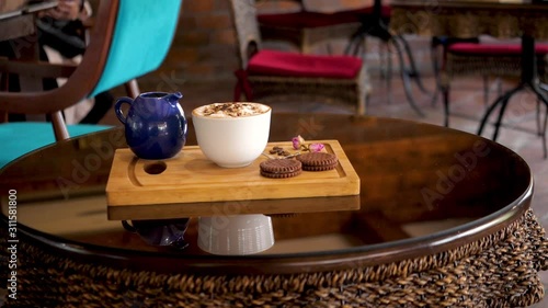 cup of Cappuccino and biscuits on  cafe table  slow-motion shot decorated wooden tray on wooden table coffee beans and flower photo