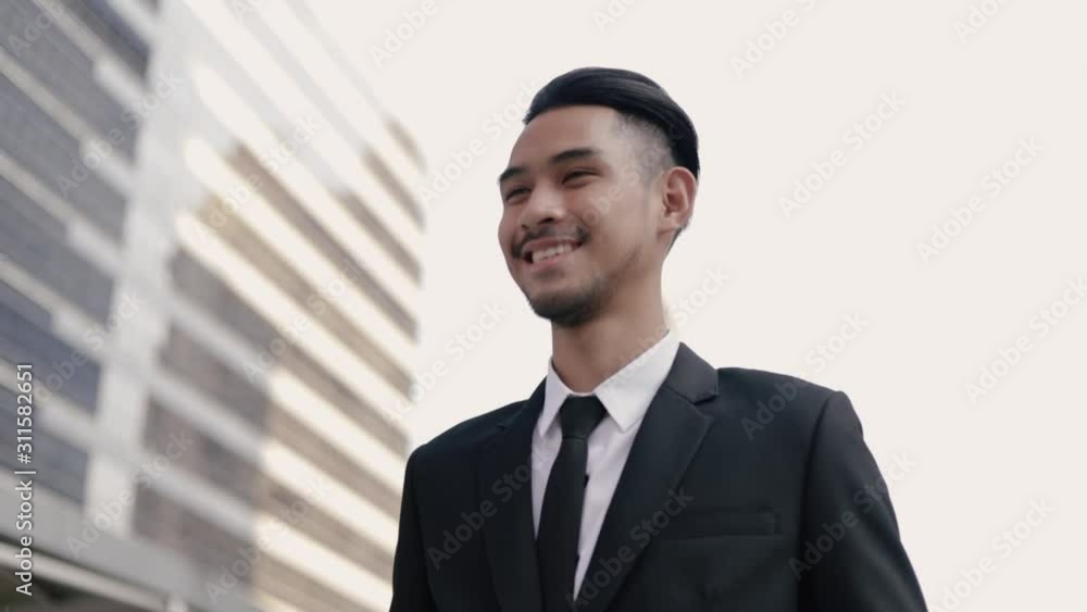 Handsome businessman in a black suit smiling while standing outside on the street near a big office building urban. Handsome businessman in a black suit smiling while standing outside on the street near a big office building urban.