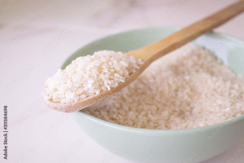  rice wooden spoon on white marble background. close-up, sprinkled rice