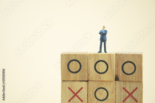 Fototapeta Naklejka Na Ścianę i Meble -  Business direction and planning concept. Businessman miniature standing and thinking on o x board games. (Tic Tac Toe). Business direction and planning concept