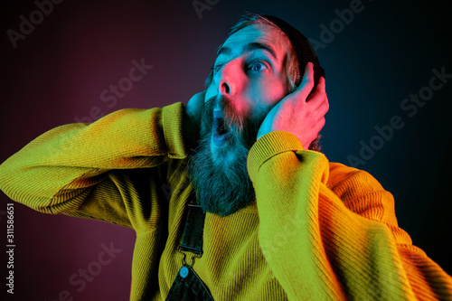 Exremely shocked, astonished. Caucasian man's portrait on gradient studio background in neon light. Beautiful male model with hipster style. Concept of human emotions, facial expression, sales, ad. photo