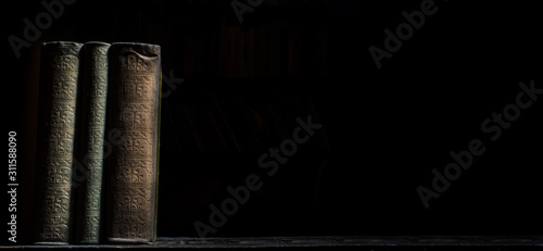 Old book on wooden bookshelf over black background. Vintage book covers still life on dark backdrop.