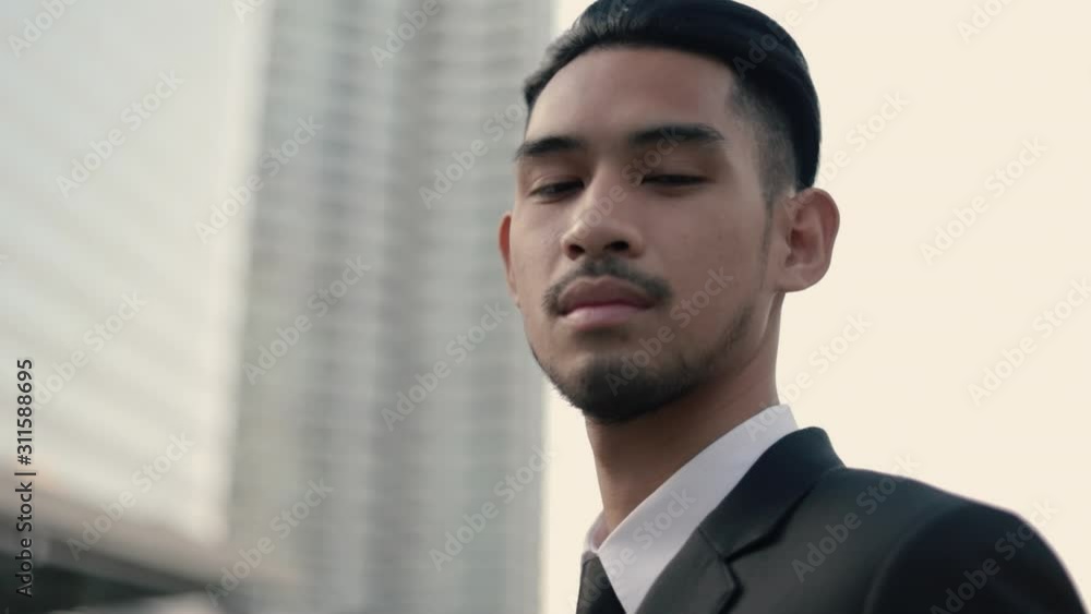 Portrait of a smiling handsome businessman in a black suit while standing outside on the street near big office building urban having sunlight sunset.