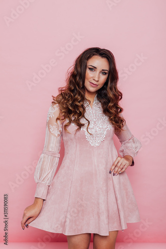 Portrait of a beautiful fashionable woman with haircurls in a pink holiday dress