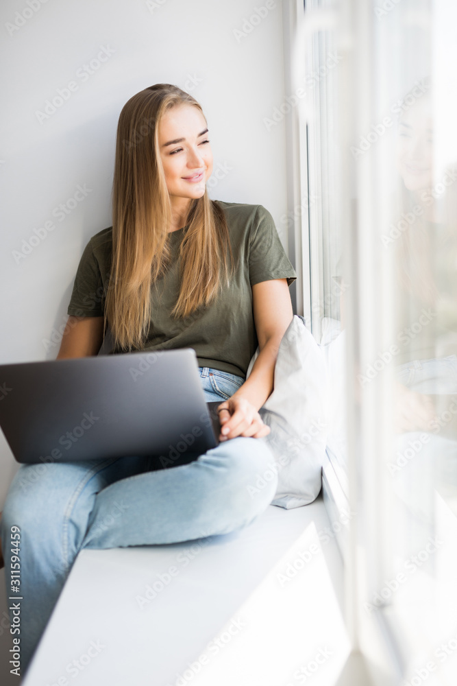Beautiful young woman sitting on a windowsill with laptop Beautiful young woman sitting on a windowsill with laptop