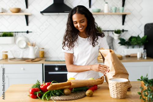 Photography Smiled beautiful girl is putting packages with  food on the table on the modern