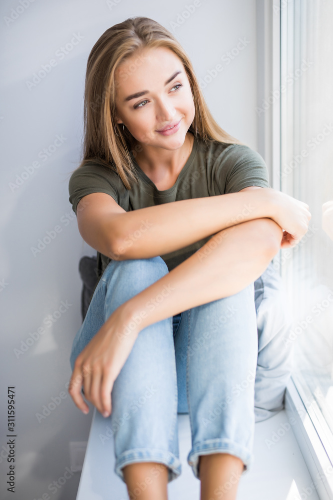 Beautiful young woman sitting at windowsill at home Beautiful young woman sitting at windowsill at home