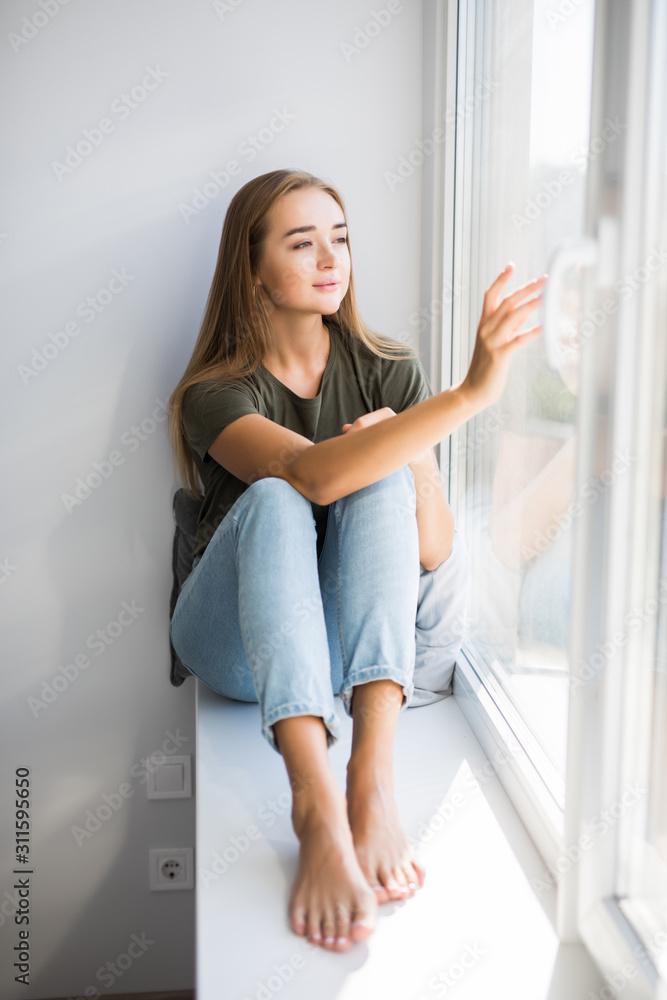 Young woman is opening window while sitting on windowsill Young woman is opening window while sitting on windowsill