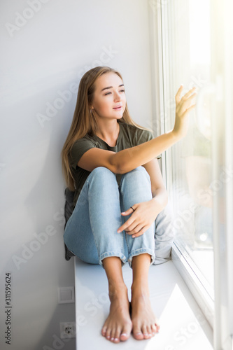 Young woman is opening window while sitting on windowsill