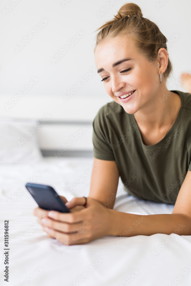 Relaxed young woman at home reading a text message in her bed Relaxed young woman at home reading a text message in her bed