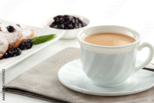 A Cup of coffee with milk and a plate with a pancakes is on the table.