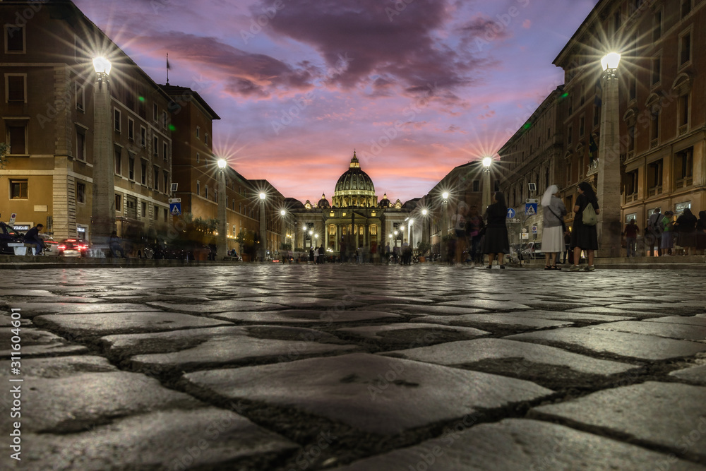 Cobbestone street lit up at dusk with view of Saint Peter's Square in the Vatican