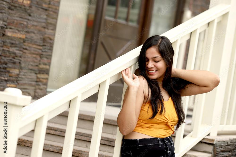 Young teenage Girl  wearing yellow top and black skirt Posing with Stair Railing outside of House in City 