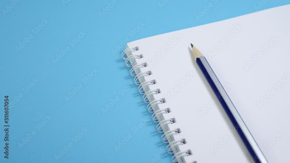 Paper notepad with pencil on blue background. Spiral notebook on table. Office supplies or education concept Paper notepad with pencil on blue background. Spiral notebook on table. Office supplies or education concept