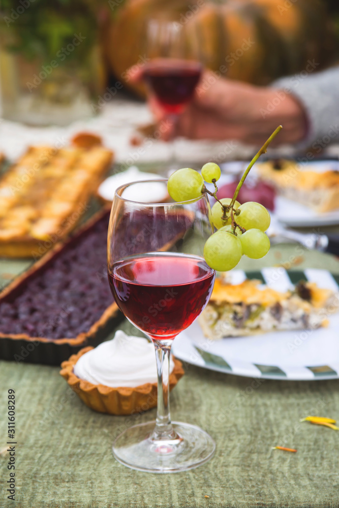 A glass of wine on a festive table in the garden on a background of pies, and the hands of an elderly woman. Family holiday concept. A glass of wine on a festive table in the garden on a background of pies, and the hands of an elderly woman. Family holiday concept.