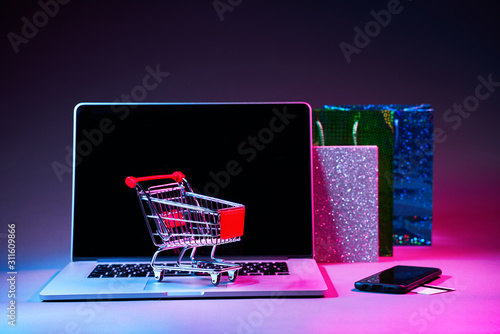 Laptop with custumers trolley, gift packet, phone and pay card on the table in modern neon colors. photo