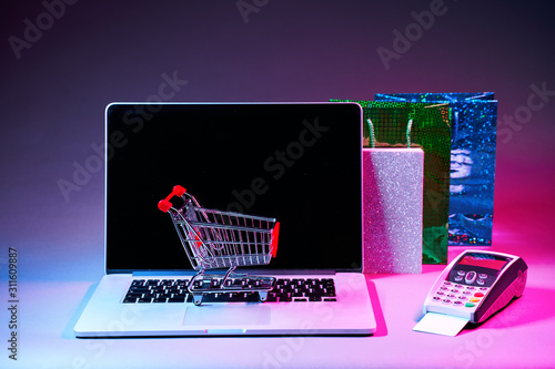 Laptop with custumers trolley, gift packet, and pin pad on the table in modern neon colors. photo