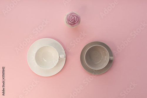 Two empty cups and rose candle on a pink background.