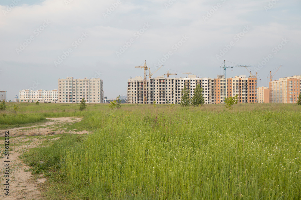 Road through green grass to construction site with houses in a new residential complex
