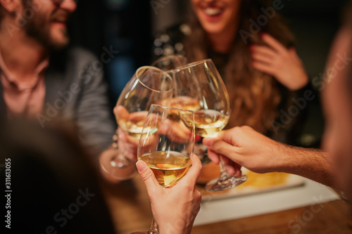 Canvas Print Best friends sitting in restaurant for dinner and making a toast with white wine
