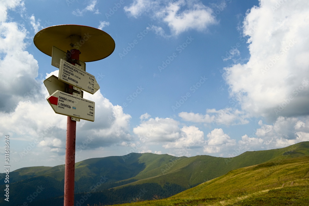 Directional sign post in the mountains with peak names and arrows with translation on English showing . trail direction on the mountain range. Carpathians, Ukraine