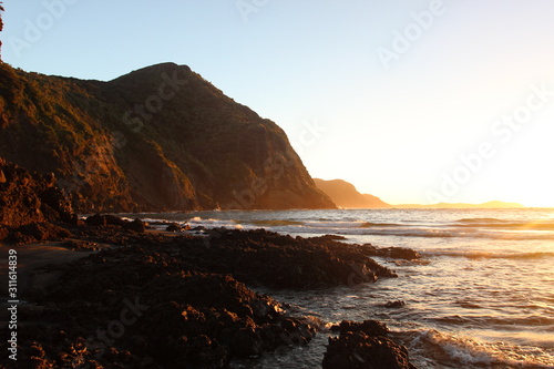 A golden sunrise from Whatipu Beach towards the cliffs and Manukau Harbour in Auckland, New Zealand.