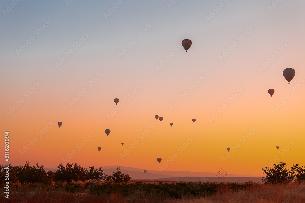 Many colorful balloons fly over the mountains - a panorama of Cappadocia at dawn. Goreme Valley Landscape in Cappadocia - Background for your travel concept in Turkey.