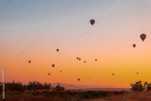 Many colorful balloons fly over the mountains - a panorama of Cappadocia at dawn. Goreme Valley Landscape in Cappadocia - Background for your travel concept in Turkey.