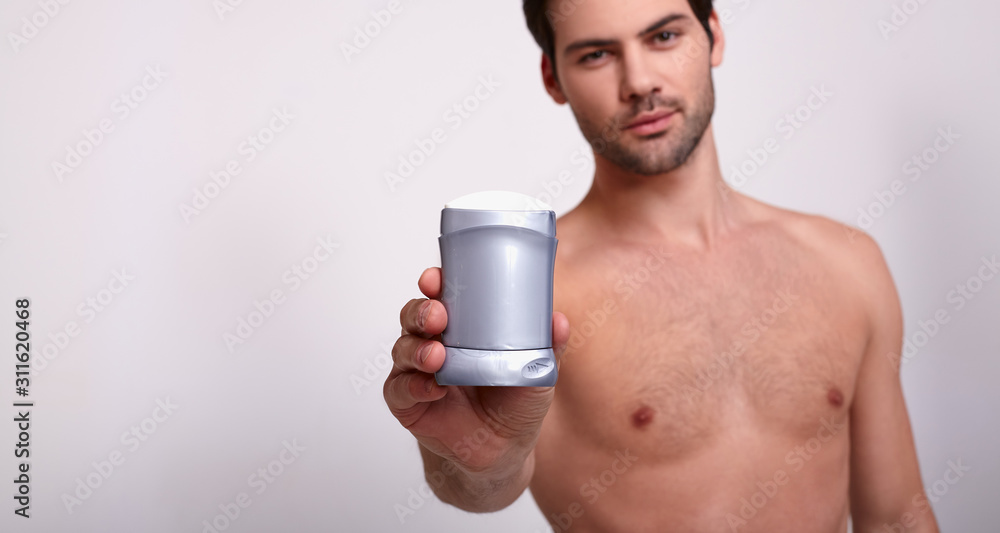 Brutal beauty strong guy holds in his right hand gray deodorant and looks at frame