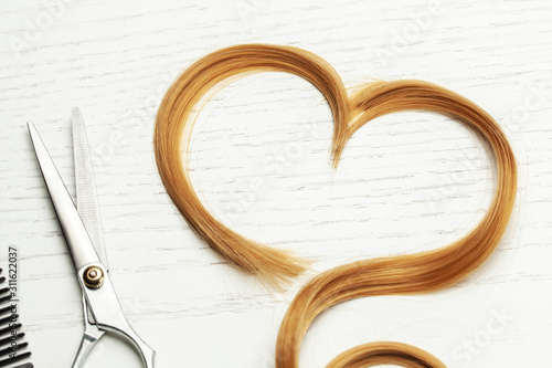 Heart made of cut hair curl and scissors. White wooden background photo