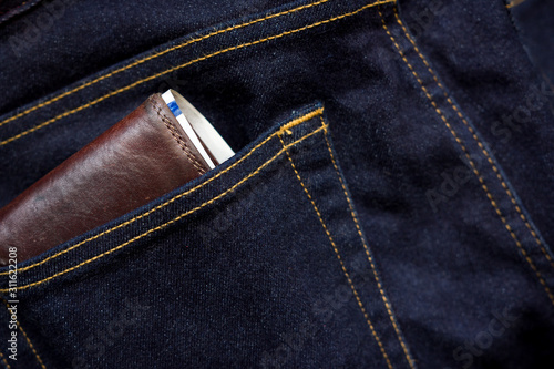 Wallet and usd banknote showing in back pocket of jeans. Selective focus on the edge of the wallet.