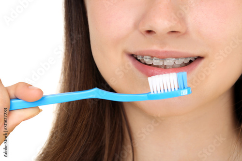 Young girl with dental braces holding toothbrush on white background