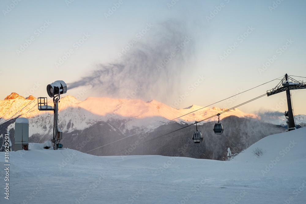 Obraz premium Snow cannon on the background of evening mountains and cable car. Preparation for the ski season.