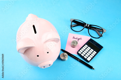 Pink piggy bank with glasses, coins and calculator on blue background