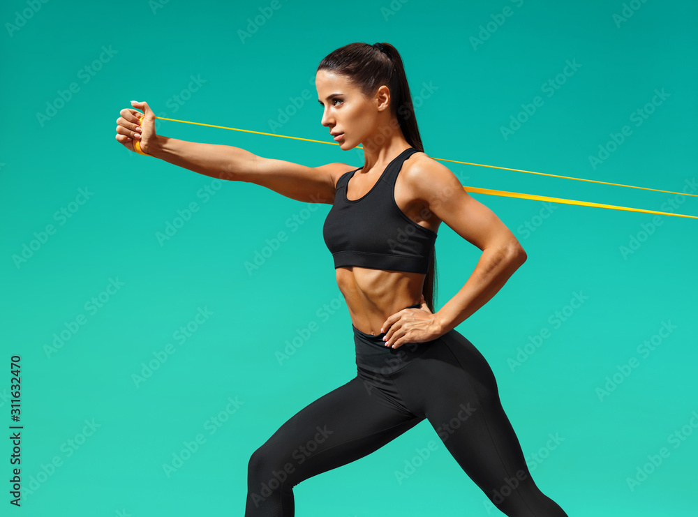 Strong woman using resistance band in her exercise routine. Photo of fitness model workout on turquoise background. Strength and motivation Stock Adobe Stock